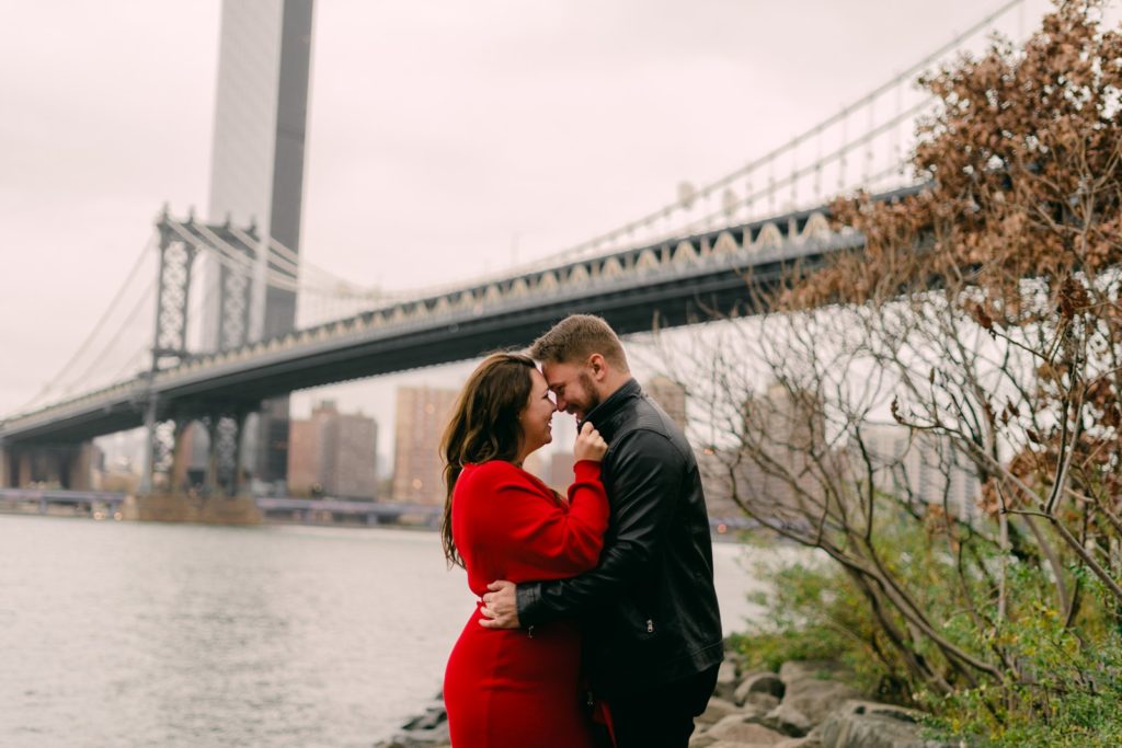 a couple posing in front of the manhattan bridge together 