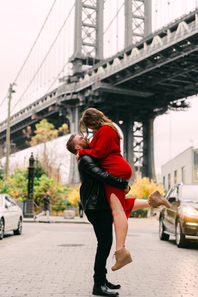 a man lifting a woman in front of the manhattan bridge