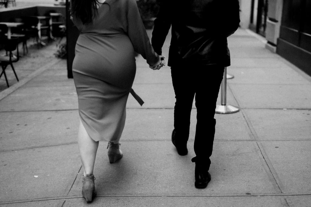a man and woman walking away holding hands on a sidewalk