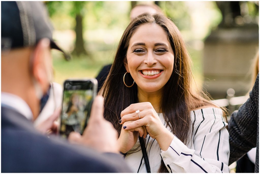 someone taking a photo of a woman smiling while holding out her hand with an engagement ring on it