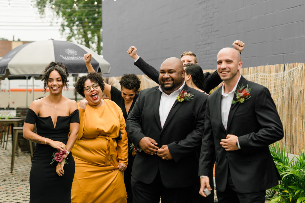 wedding party in black attire cheering and smiling in a group