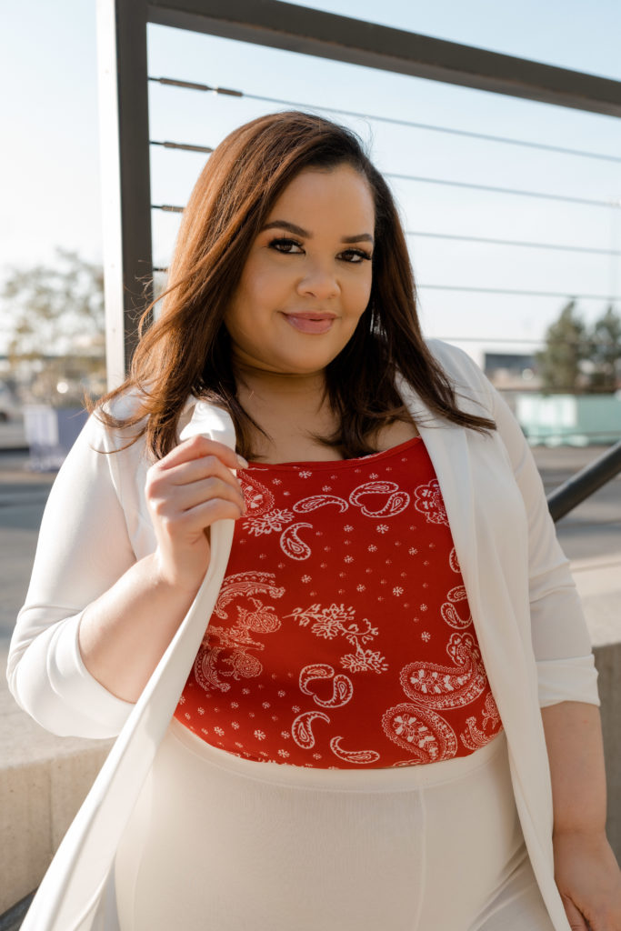 Woman wearing a patterned red shirt under a white suit. She is holding the side of her jacket with one hand