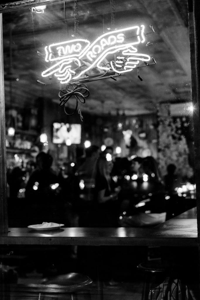 Window sign that says two roads lit up in a window of a bar