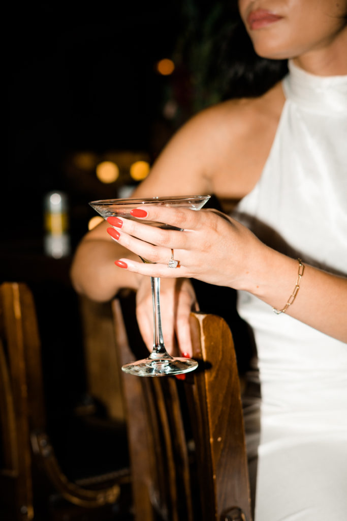 a hand with an engagement ring holding a martini glass