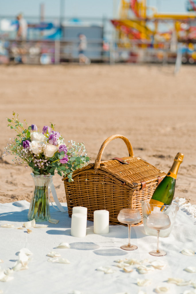 a picnic set up on the beach with flowers, champagne, and candles