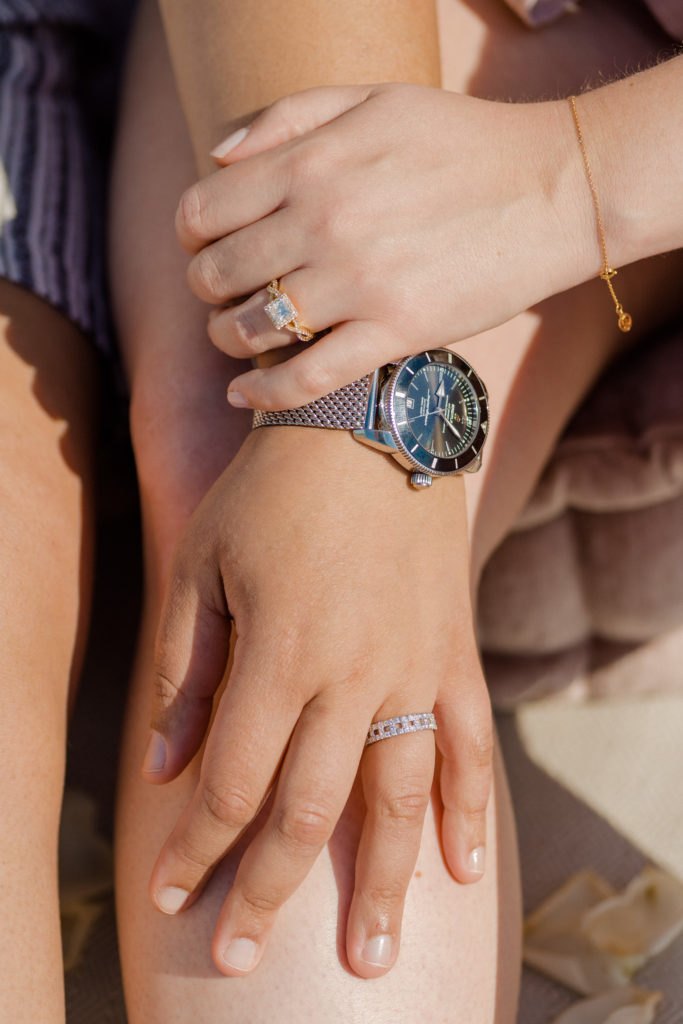two hands with engagement rings on them. One hand is resting on the wrist of the other hand.