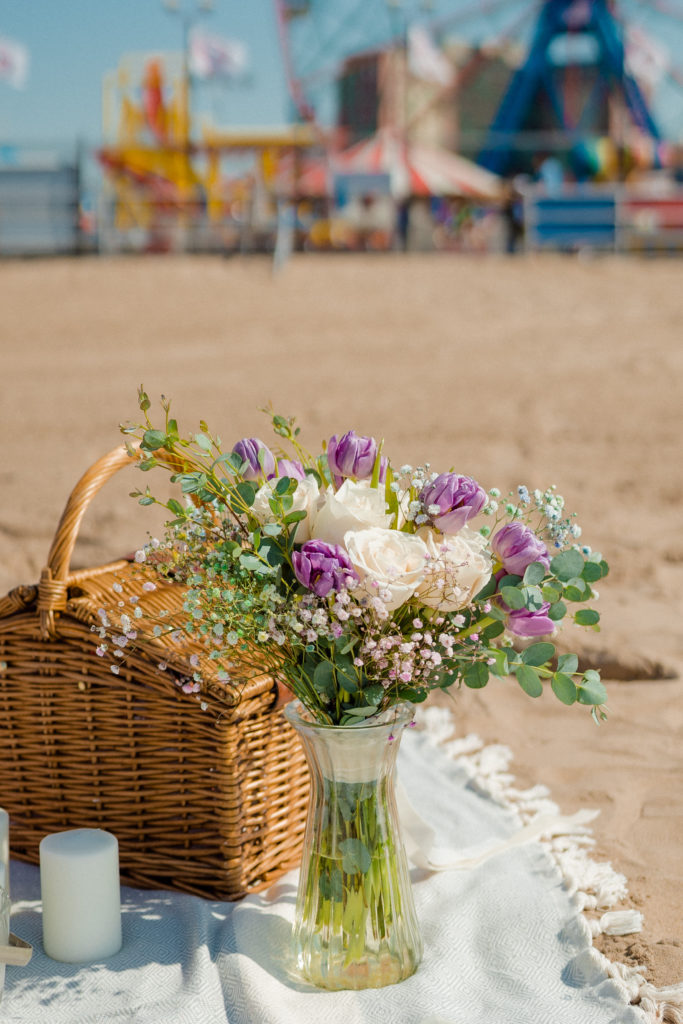 a bouquet of purple flowers in a vase on a beach blanket