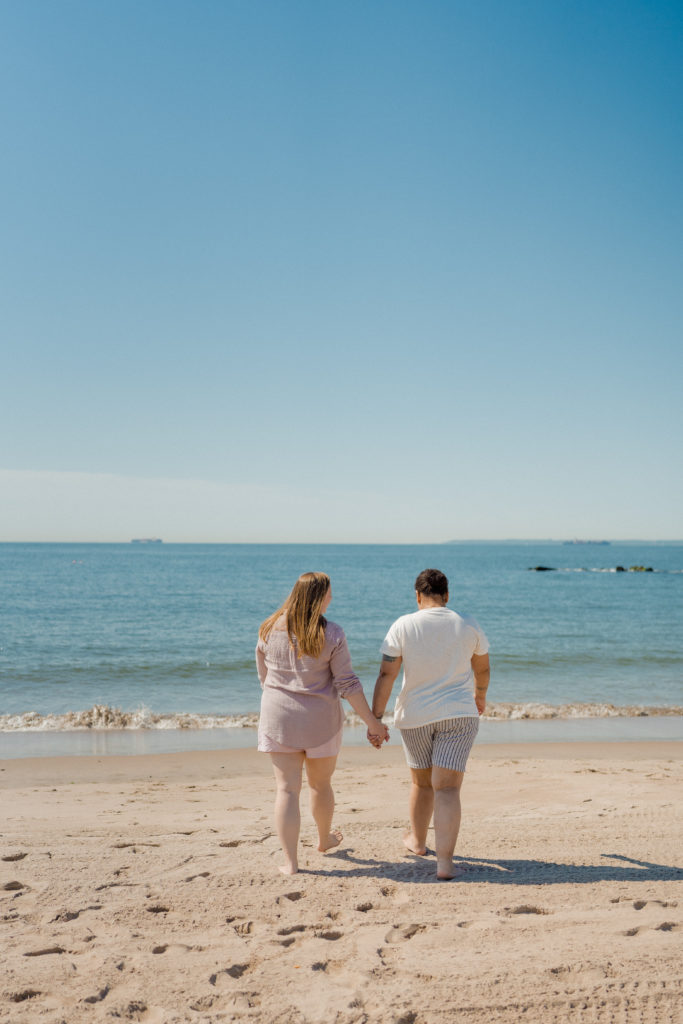 a couple holding hands as they walk towards the ocean water
