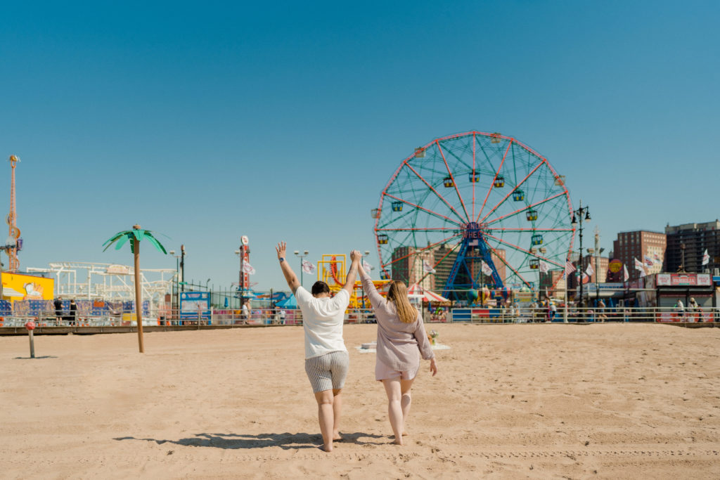 a couple raising their hands in celebration as they walk towards the coney island wonder wheel