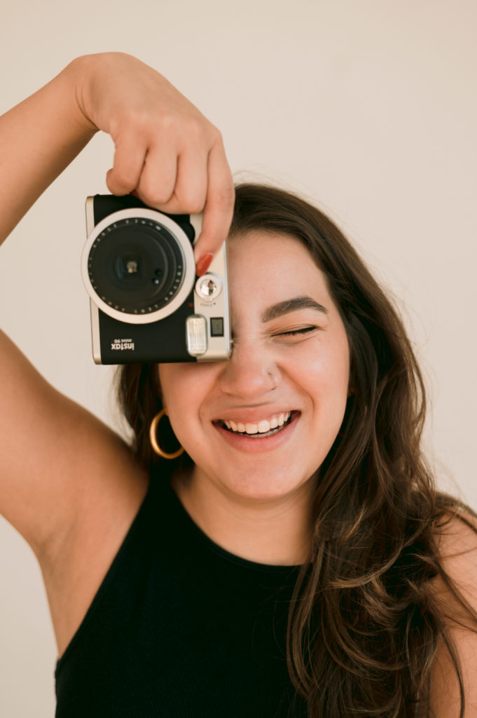 woman holding up a camera in front of one eye while laughing