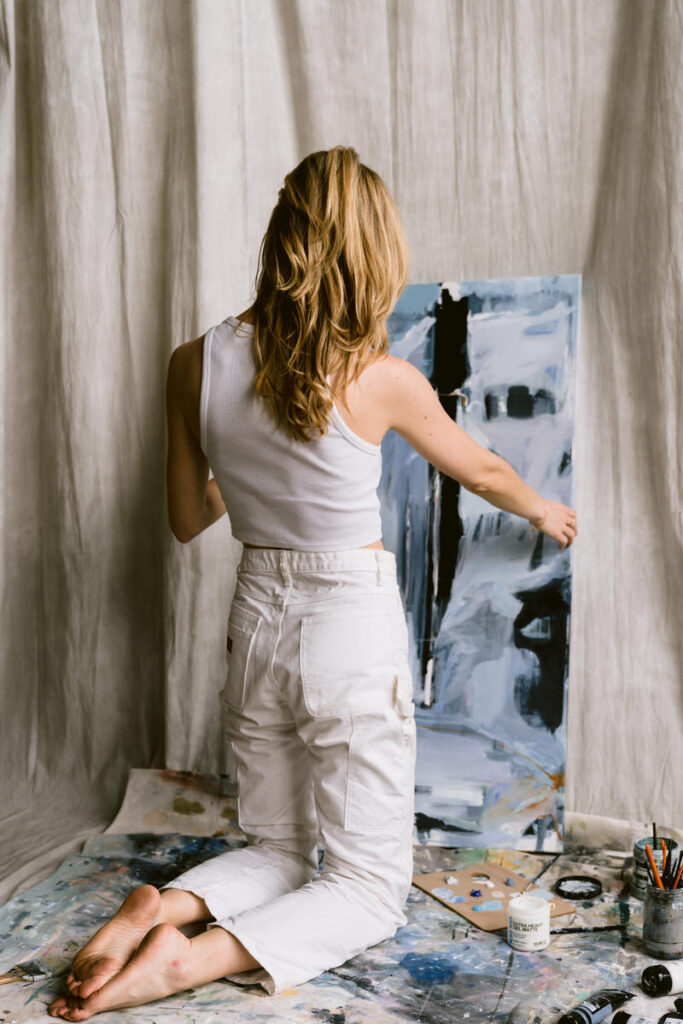 Woman kneeling down as she paints on a canvas. 