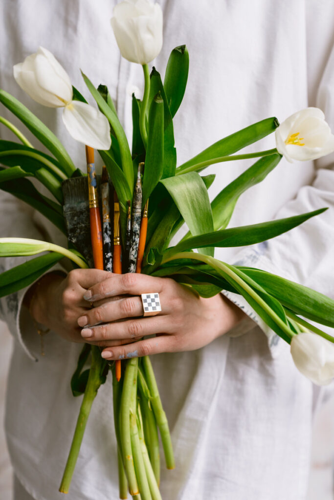 Hands holding a bouquet of flowers and paintbrushes. 