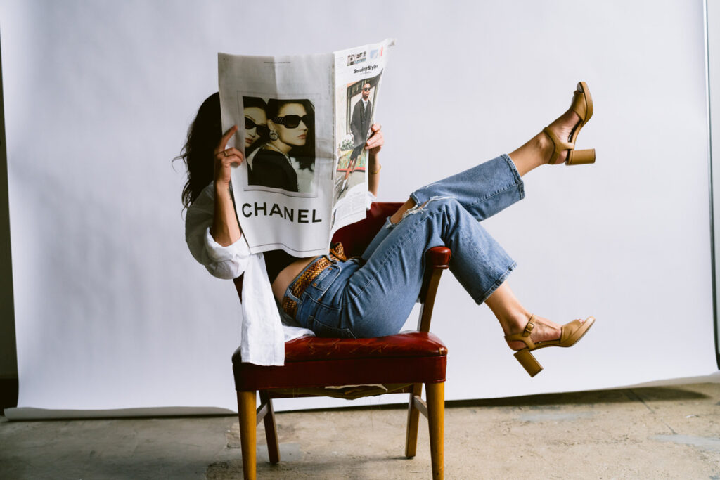 Woman sitting sideways in a chair holding up a newspaper. 