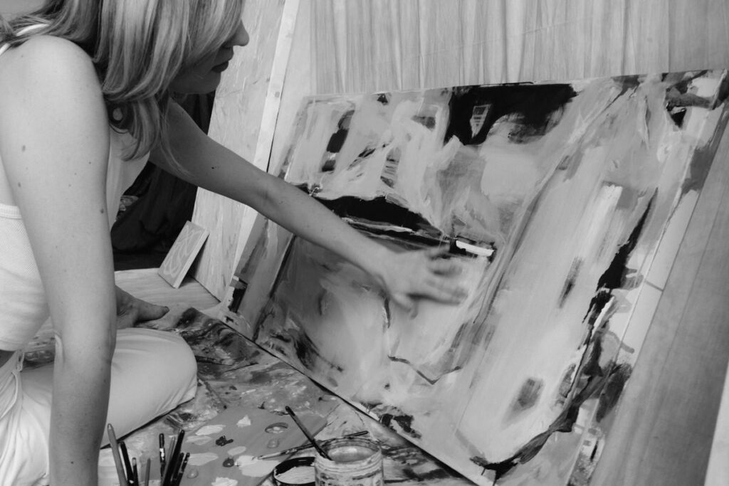A black and white photo of an artist painting on a canvas. 
