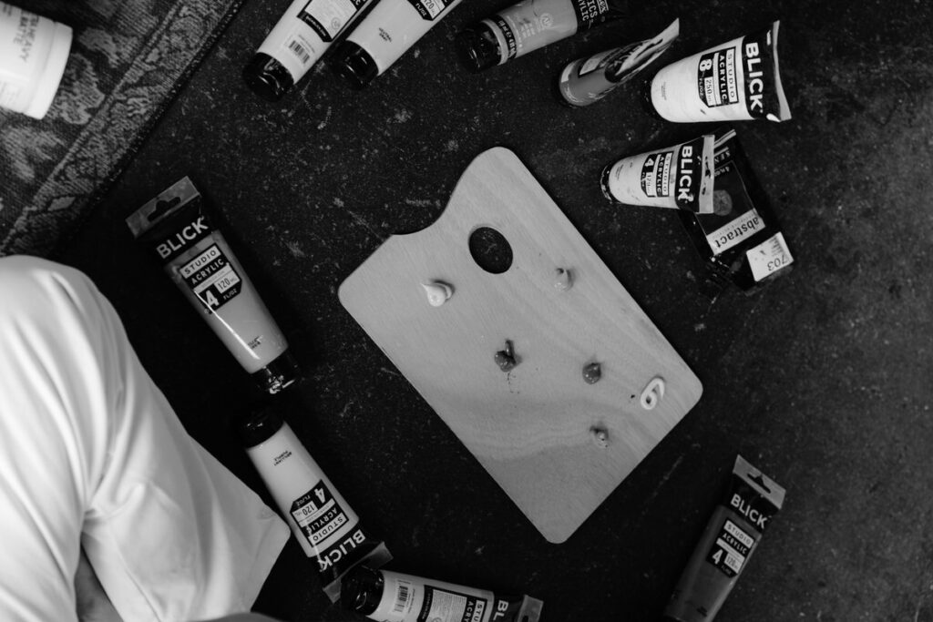 A black and white image of bottles of paint laid out next to a palette. 
