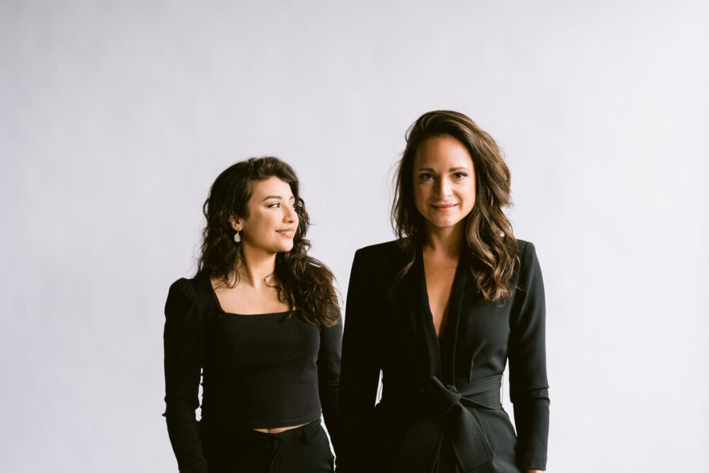 Two women in black suits standing next to each other. 