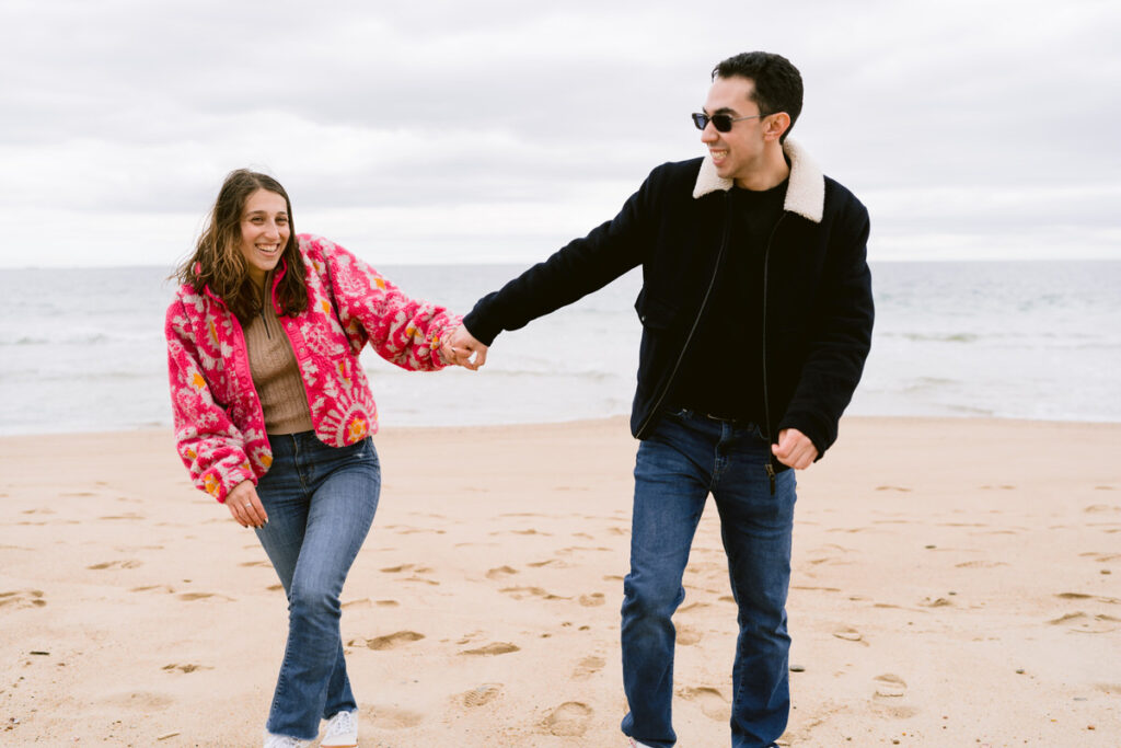 A couple holding hands and walking up a beach. 
