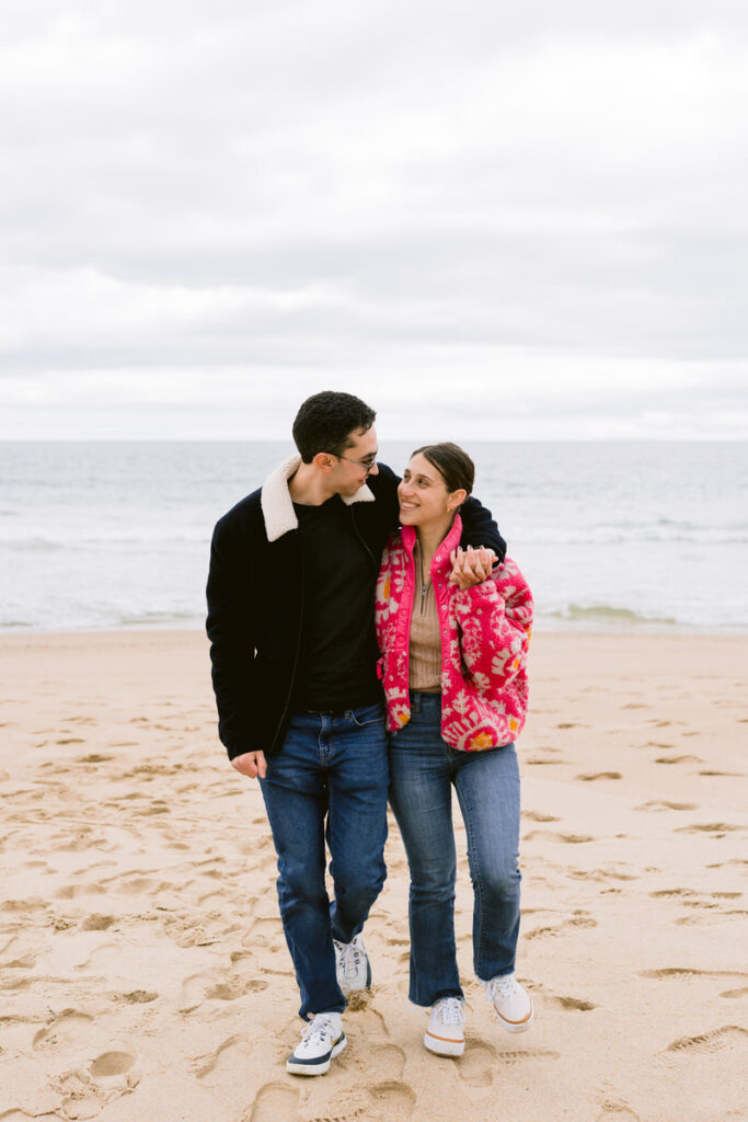 A couple with their arms around each other as they walk along a beach. 