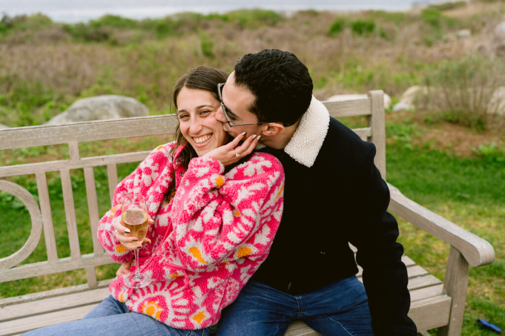 A person kissing their partner's cheek as they sit on a bench. 
