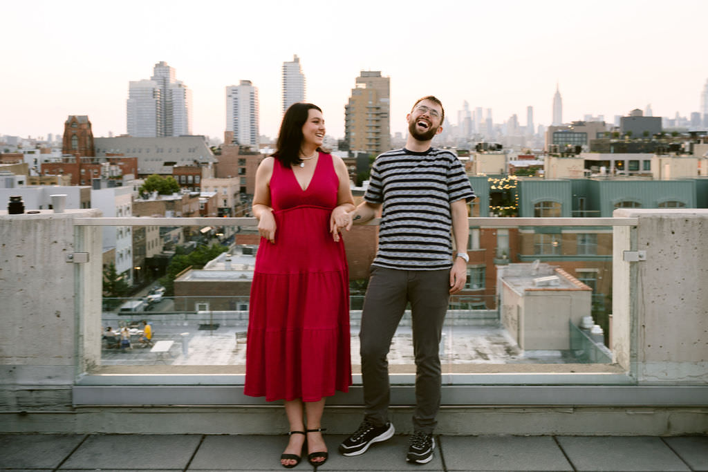 A couple standing on a rooftop with the NYC skyline behind them. 