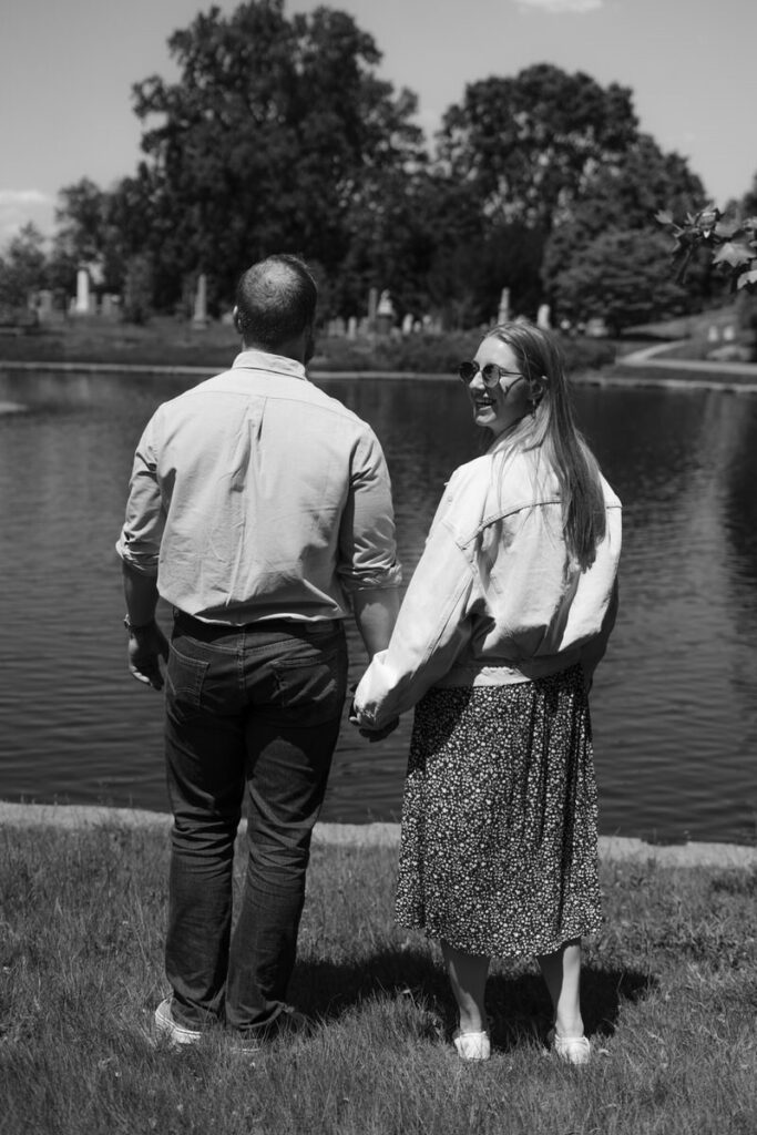Black and white photo of a couple holding hands and walking along a lake. 