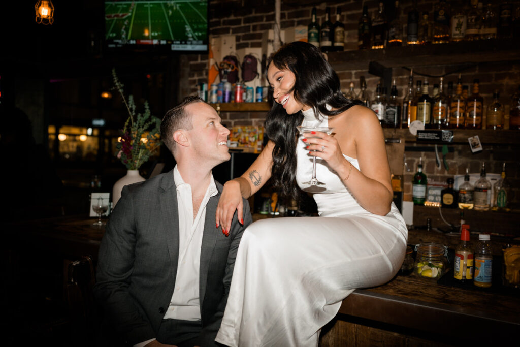 A person sitting a bar holding a martini glass while leaning down on her partner's shoulder. 