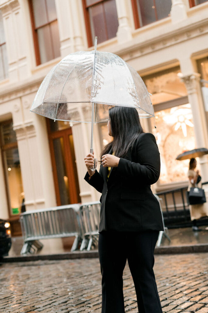 A woman looking back over her shoulder as she crosses the street while holding a clear umbrella. 