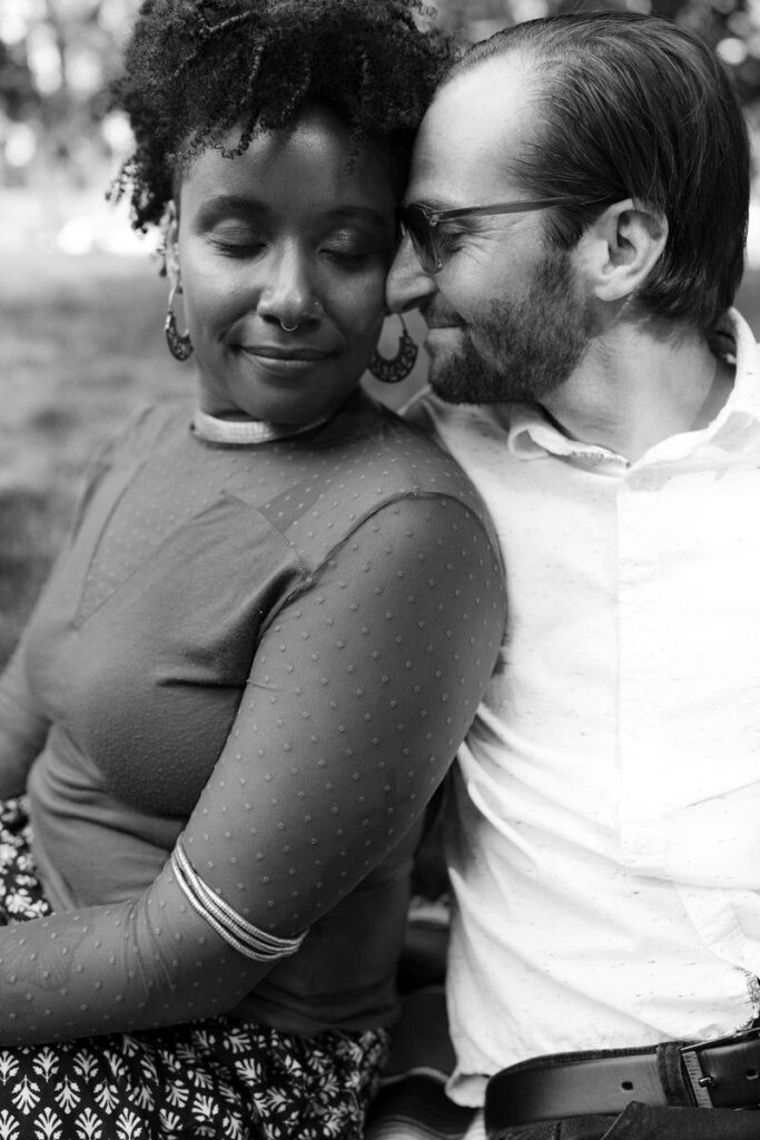 Black and white photo of a woman leaning back into her partner as he rests his head on hers. 