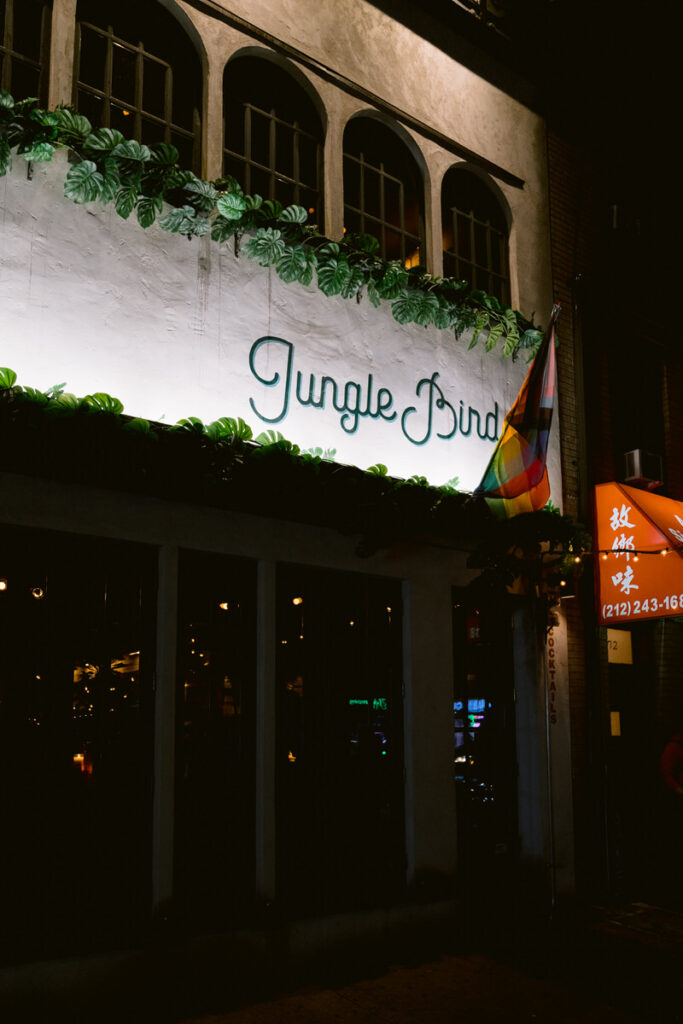 The outside of a restaurant with the words "Jungle Bird" lit up on the side. 