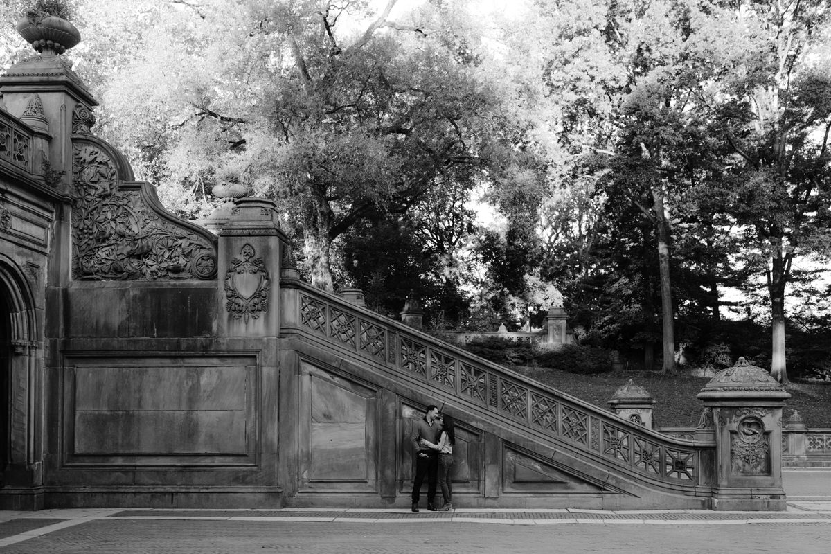 Engagement Photos in Central Park of a couple standing against the wall of an outdoor staircase in a plaza.