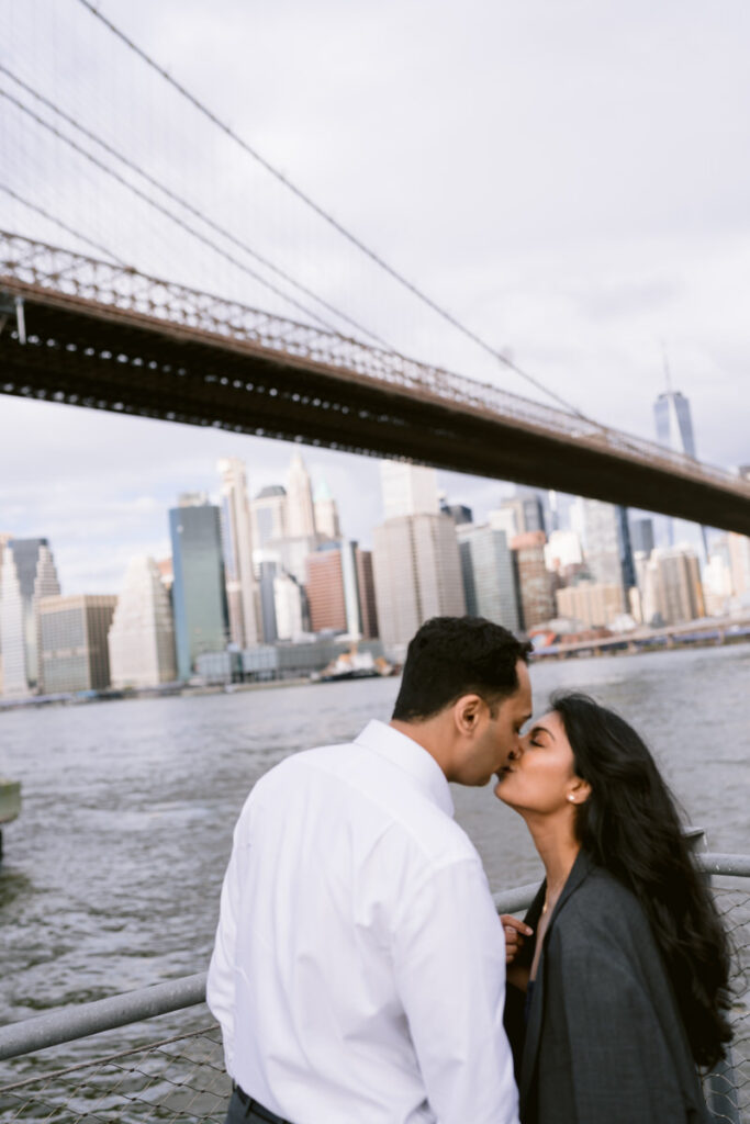 A couple kissing with the New York City skyline in the distance. 
