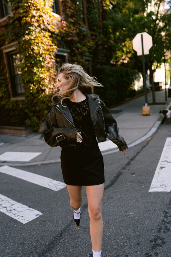 A woman in a lively stride wearing a black leather jacket and mini skirt, her hair caught in mid-motion, embodies the energy of city life
