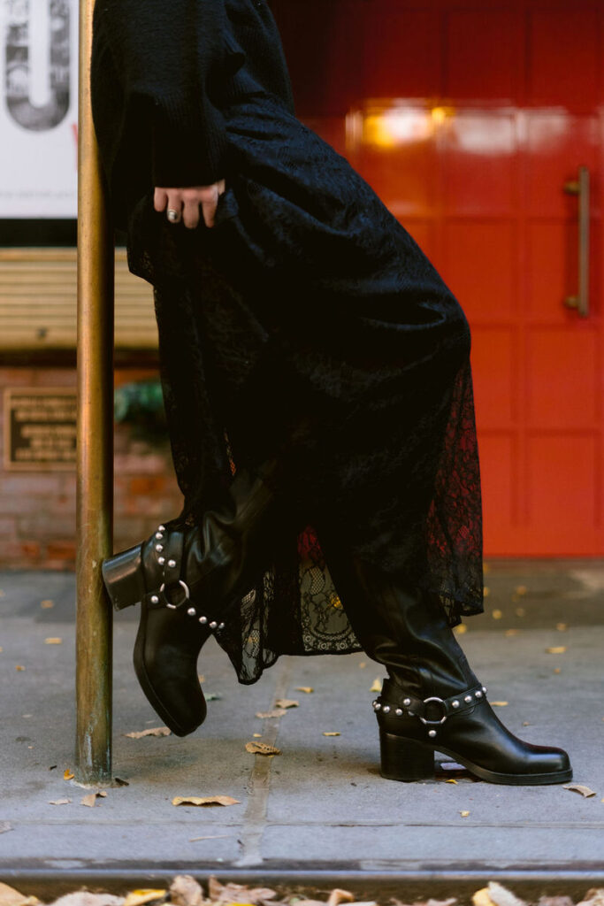 A close-up on the stylish details of a woman's black lace skirt and studded leather boots, with autumn leaves scattered around