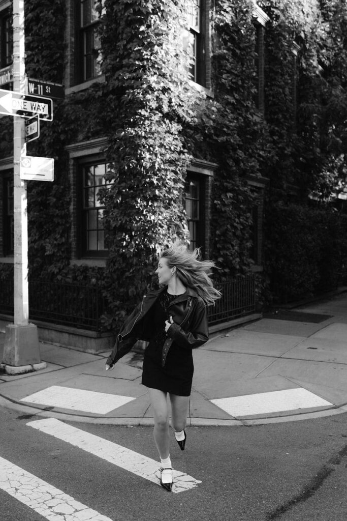 In a dynamic black and white photo, a woman's hair flutters in the wind as she crosses a street in the West Village, her joyful energy palpable