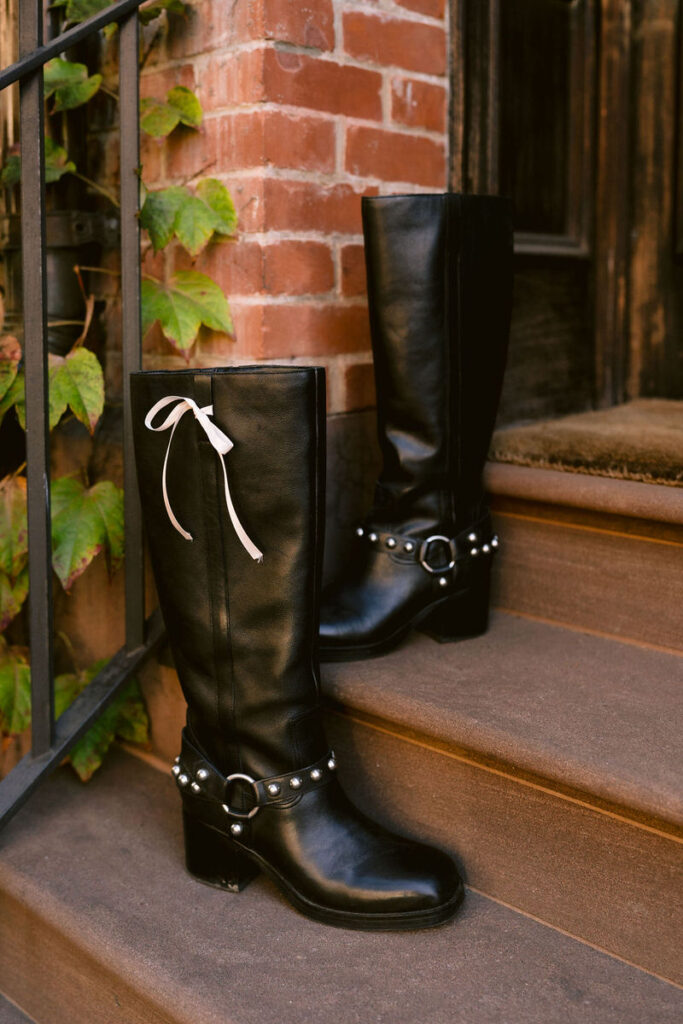 Stylish black leather boots with pearl embellishments on the steps of a brownstone, complemented by autumnal ivy, highlighting a mix of rugged and delicate fashion elements