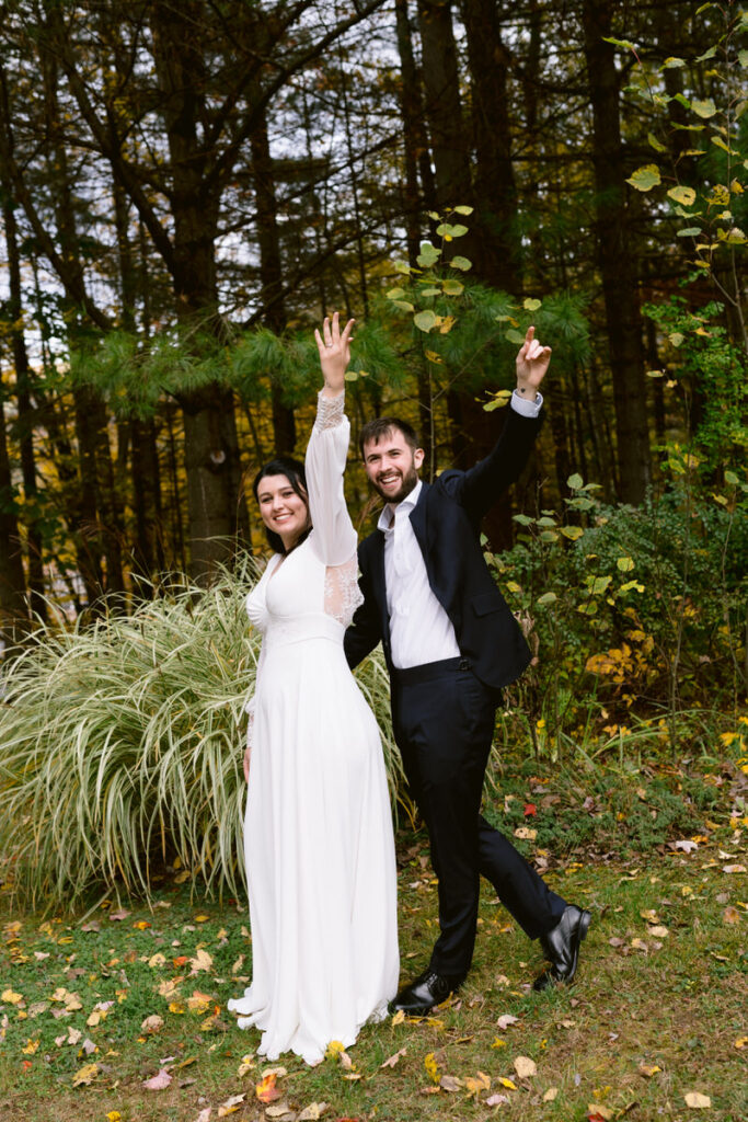 A bride and groom smiling as they both hold up one hand. 