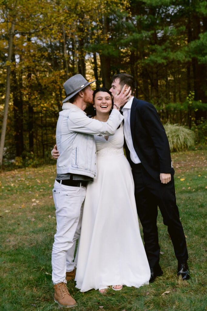 A bride with a guests on one side and her groom on the other as they both kiss her head. 