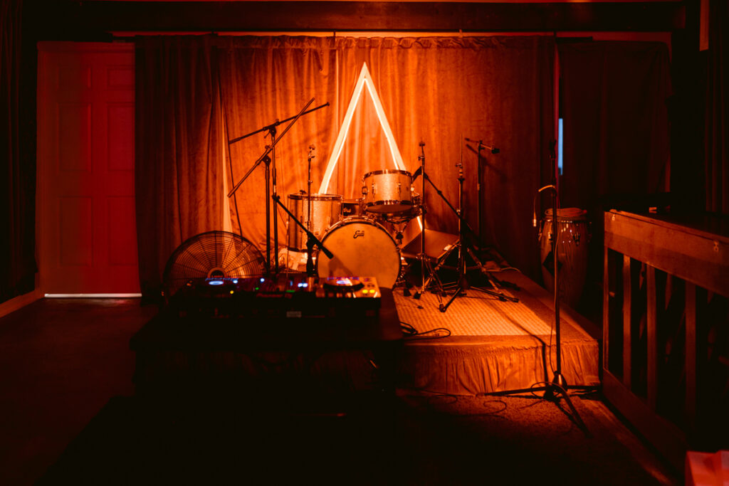 A warmly lit wedding venue stage with a drum set and musical equipment