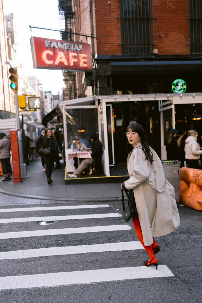 Crossing a bustling NYC street, the subject is captured in mid-stride, wearing a flowing trench coat, a zebra print skirt, and striking red tights, blending urban chic with a hint of wild flair.