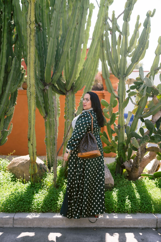 Full-body image of a person standing in a cactus garden, wearing a green polka dot kimono, denim, and holding a vintage designer handbag, radiating a relaxed and stylish vibe.