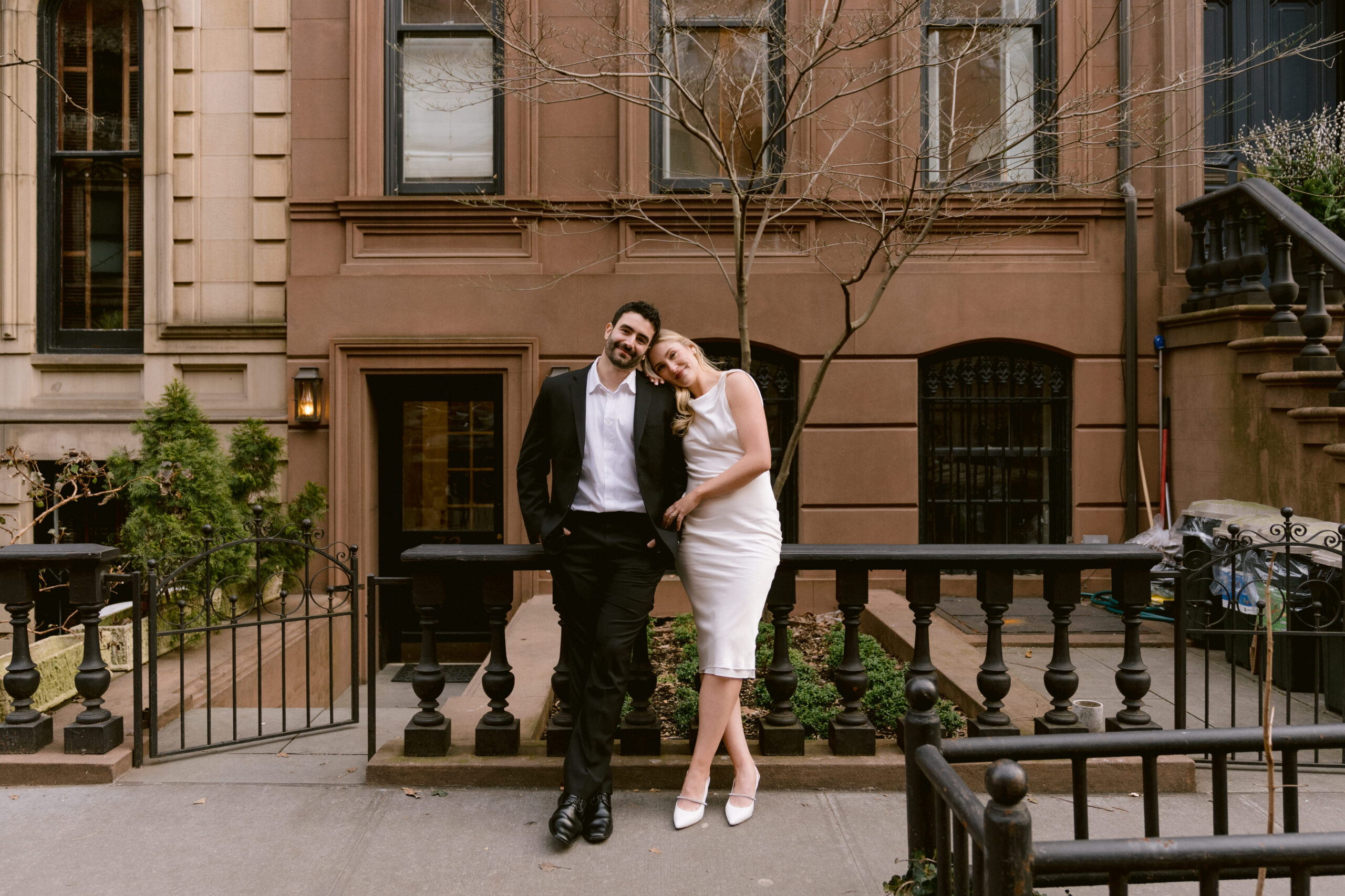 west village engagement photos of a couple holding hands and leaning back onto the front gate of a brownstone