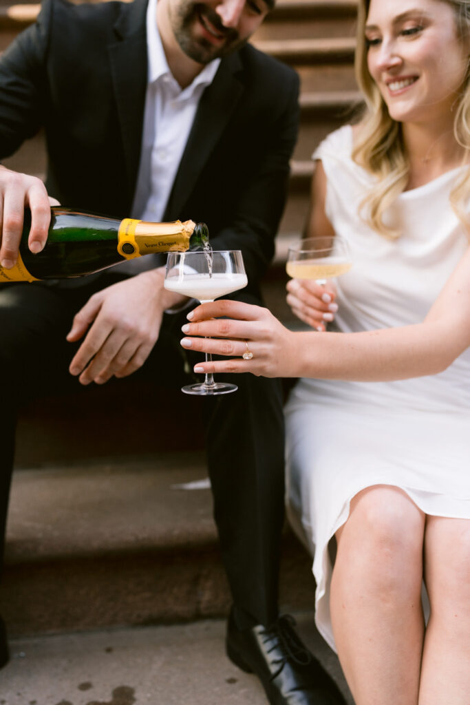 A man pours a woman a glass of champagne outdoors.