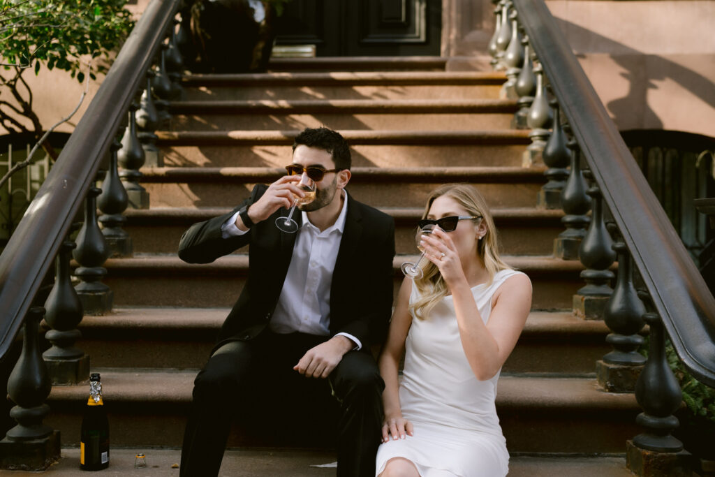 A couple drinks from champagne glasses on steps outdoors.