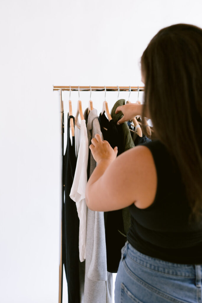 A person pulling out a piece of clothing from a rack 
