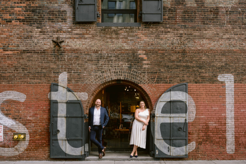 A couple leaning on either side of a doorway to a red brick building 