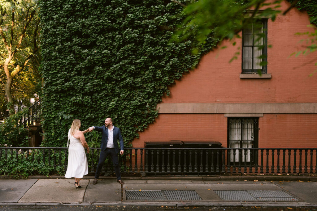 A couple dancing on a sidewalk outside of a brownstone 