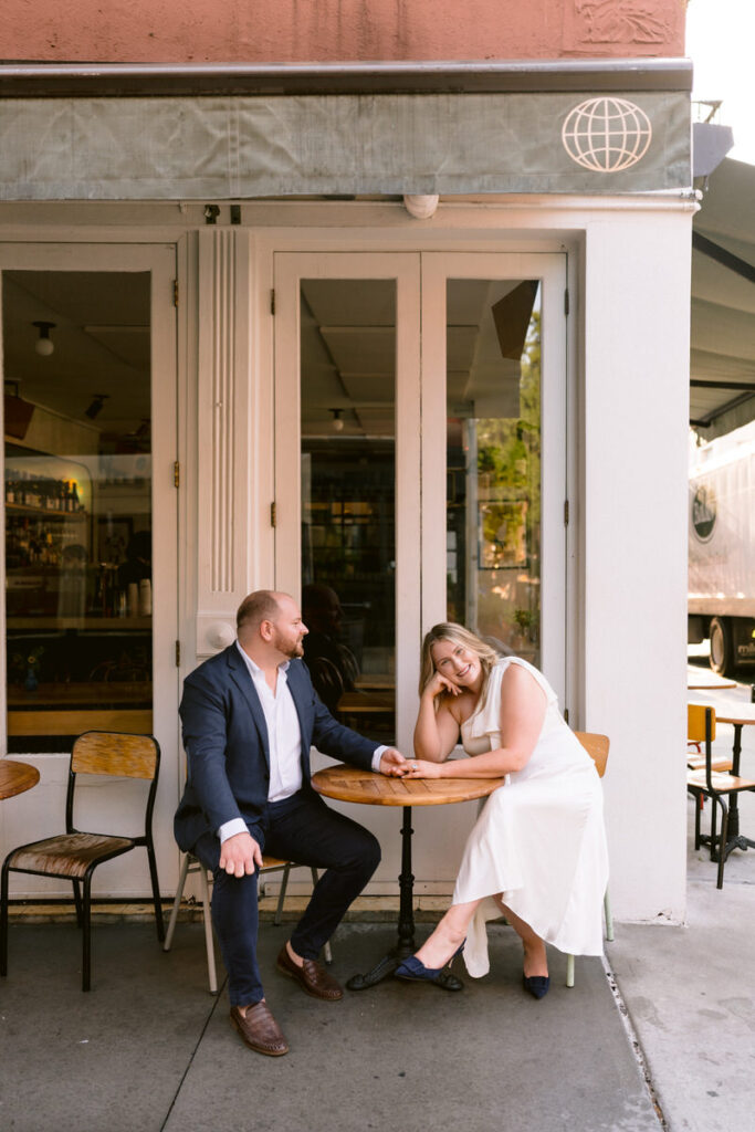 A couple sitting at a small coffee shop table holding hands 
