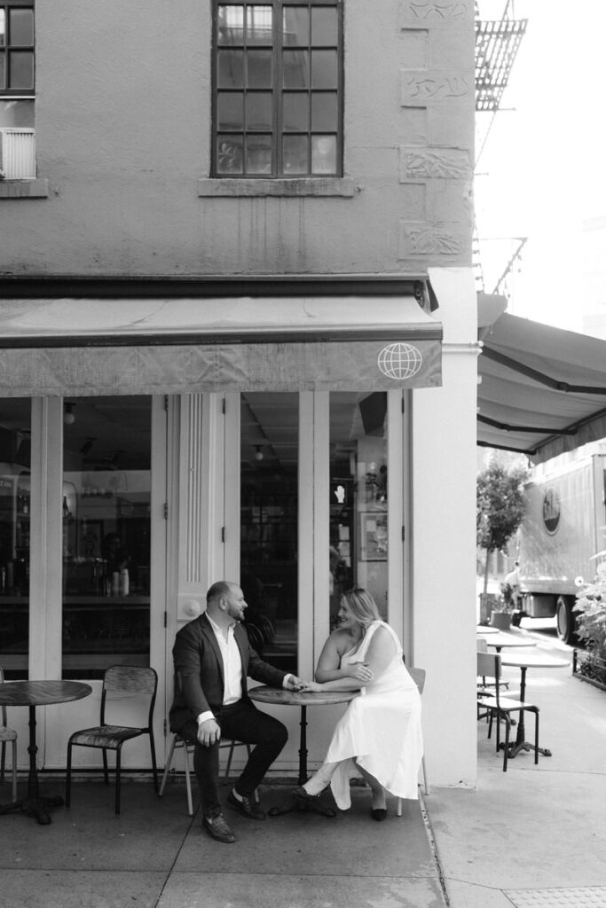 Black and white photo of a couple sitting at a table outside a cafe 