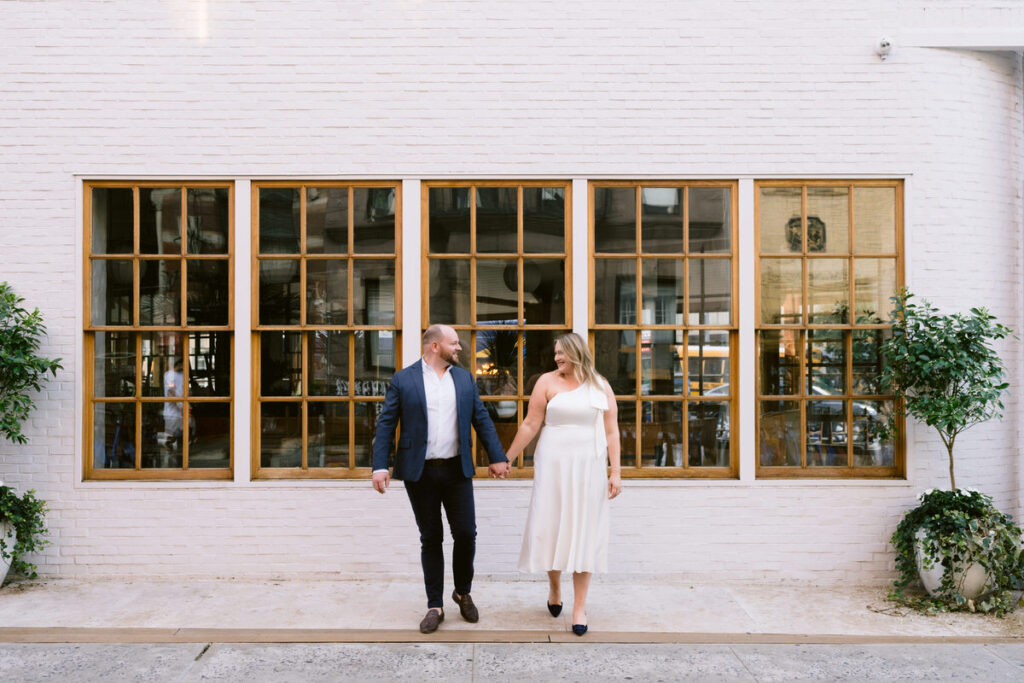 A couple holding hands and walking towards a street 
