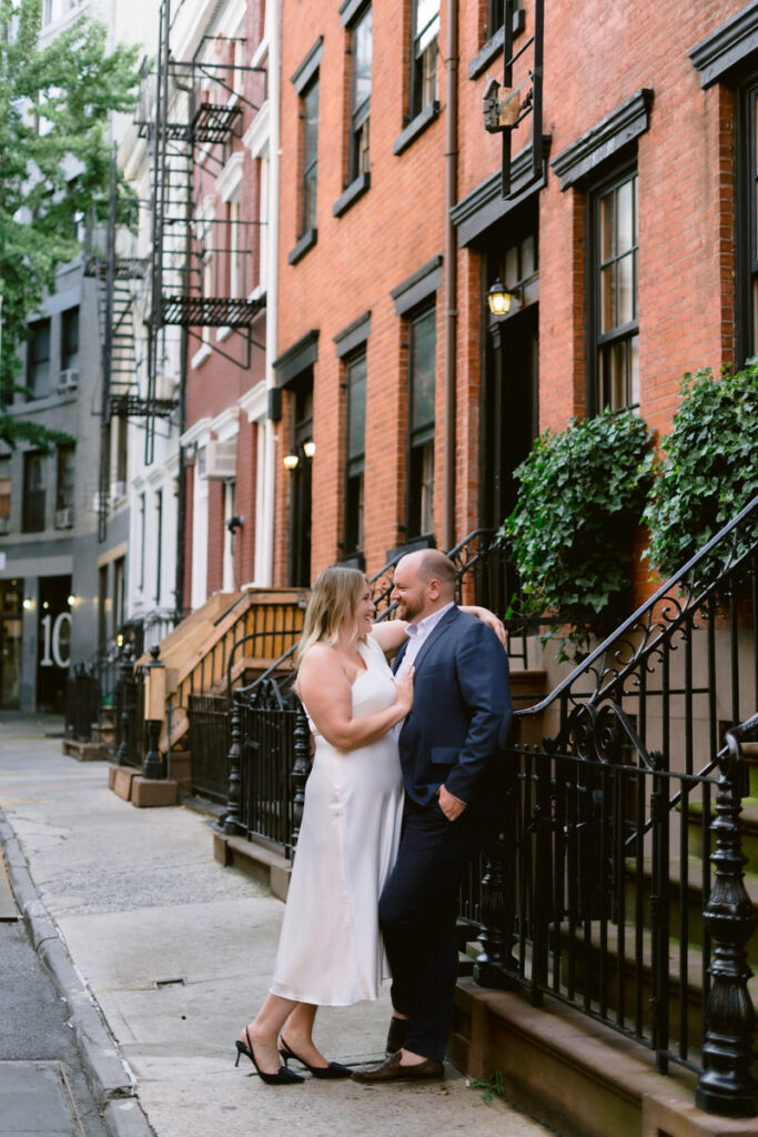 A couple standing close together and leaning on a staircase to a brownstone 
